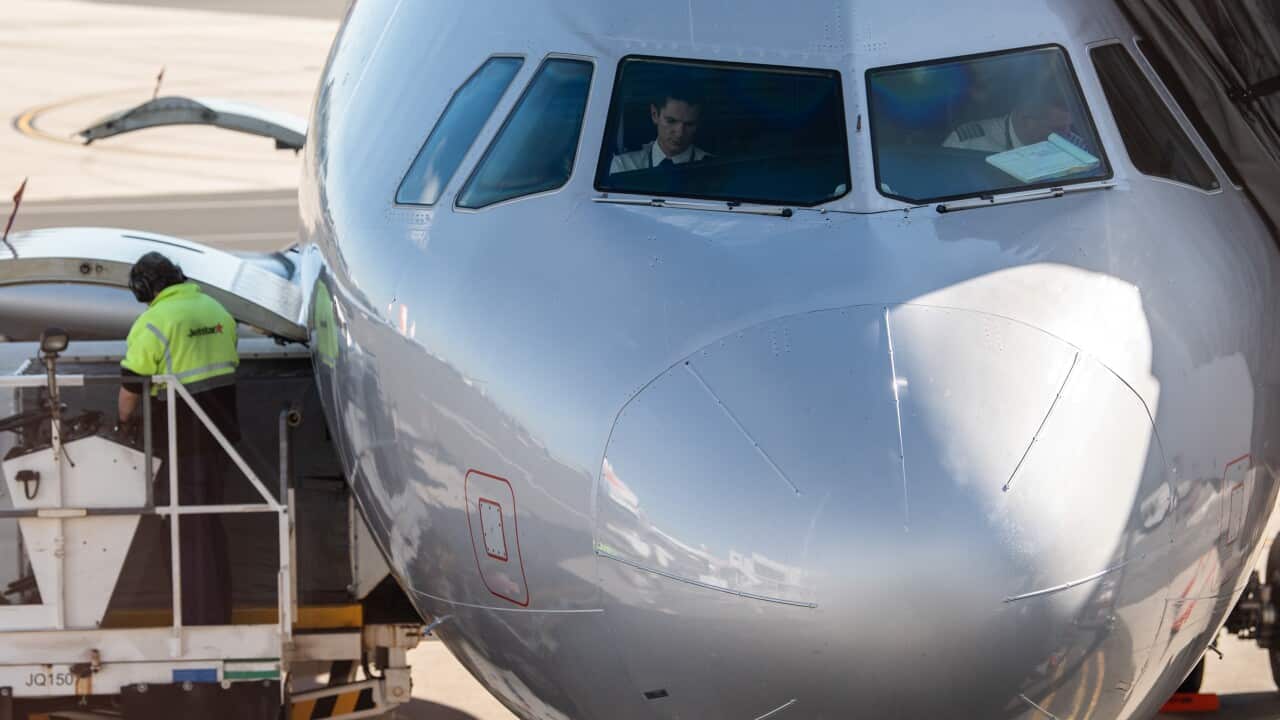 Pilots sit in the cockpit of an aircraft at an airport with an airport crew in green vest working on the left.
