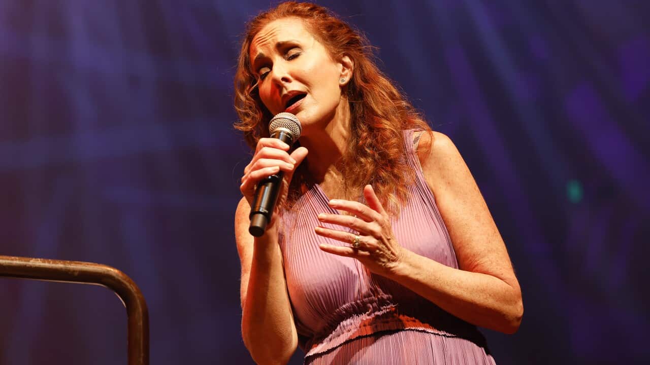 A woman with red hair closing her eyes and singing into a microphone.