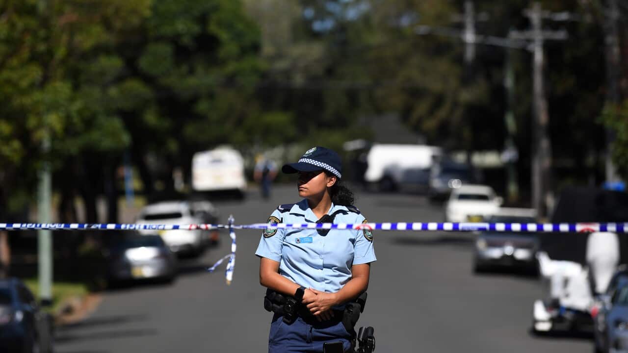 A female police officer stands behind a police tape.