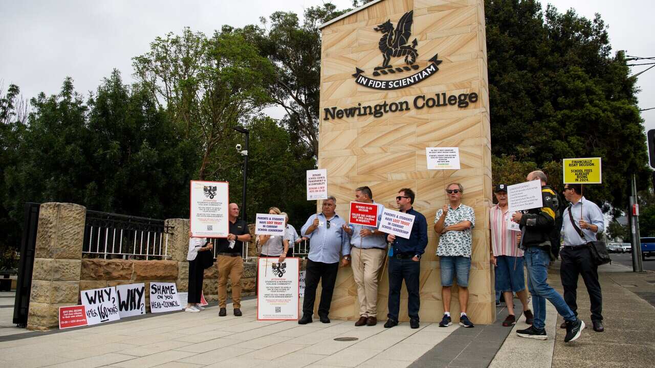 People standing in front of a sign outside a school holding placards.