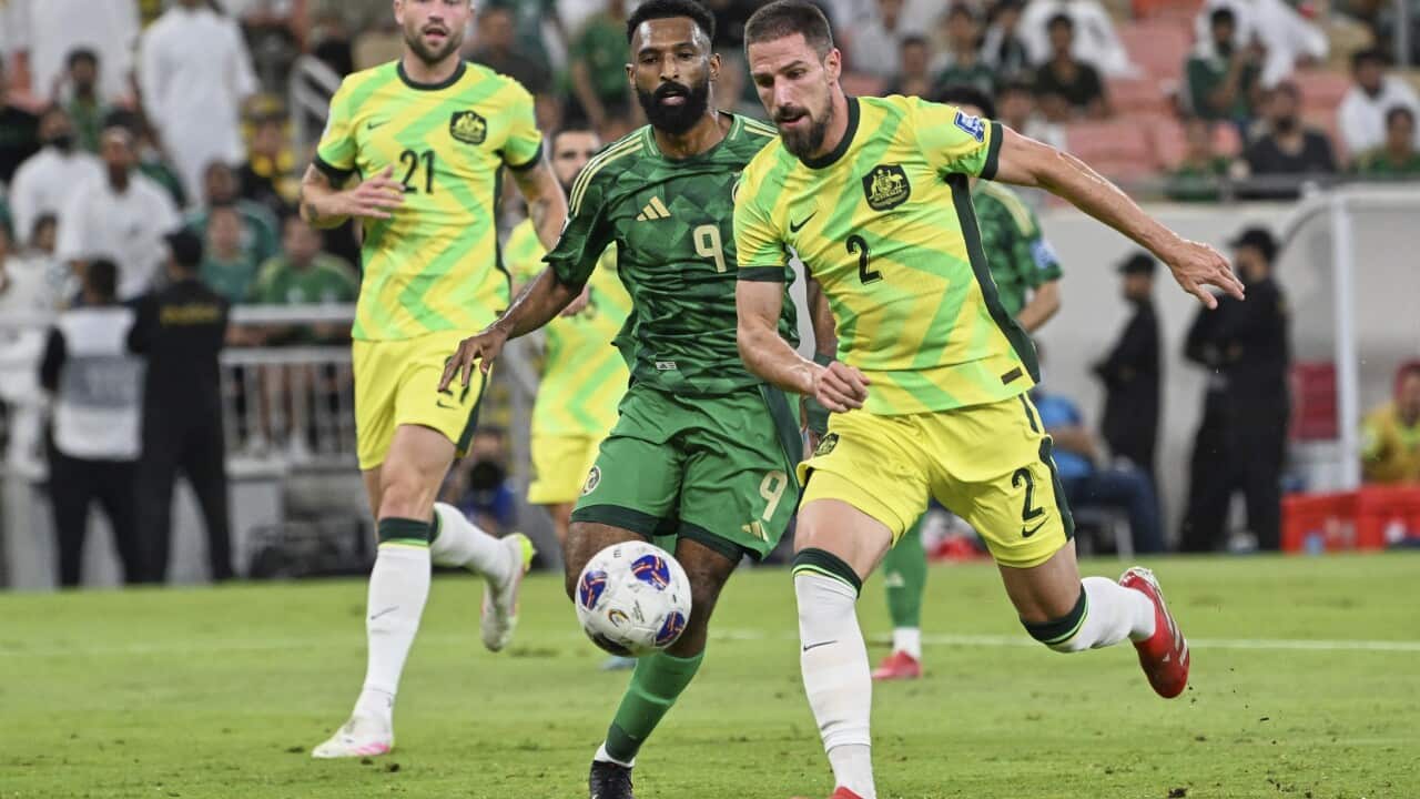 A footballer in a yellow and light green strip competes closely for the ball with a man in green strip