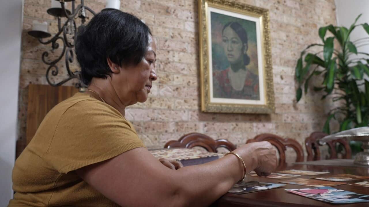 Phiny Ung looks at family photos. On the wall behind her is a portrait that her husband painted.