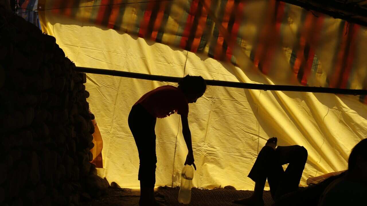 A Nepalese earthquake survivor takes a bottle of water as another lies on the floor inside a makeshift shelter at a devastated area in Bungamati, Nepal, 14 May 2015. (EPA/MAST IRHAM)