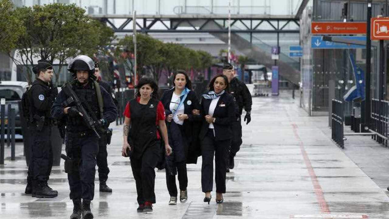 A police officer escorts airport employees outside the Orly airport , south of Paris