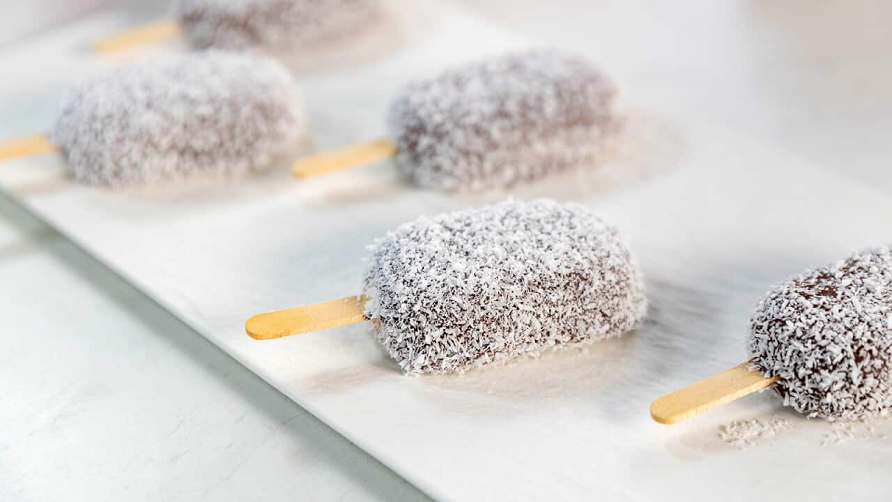 Two rows of chocolate and coconut coated icecreams, with wooden paddle pop stickes, sit on a white platter.