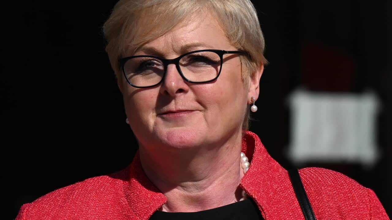 A woman wearing glasses, a black top, and a red blazer.