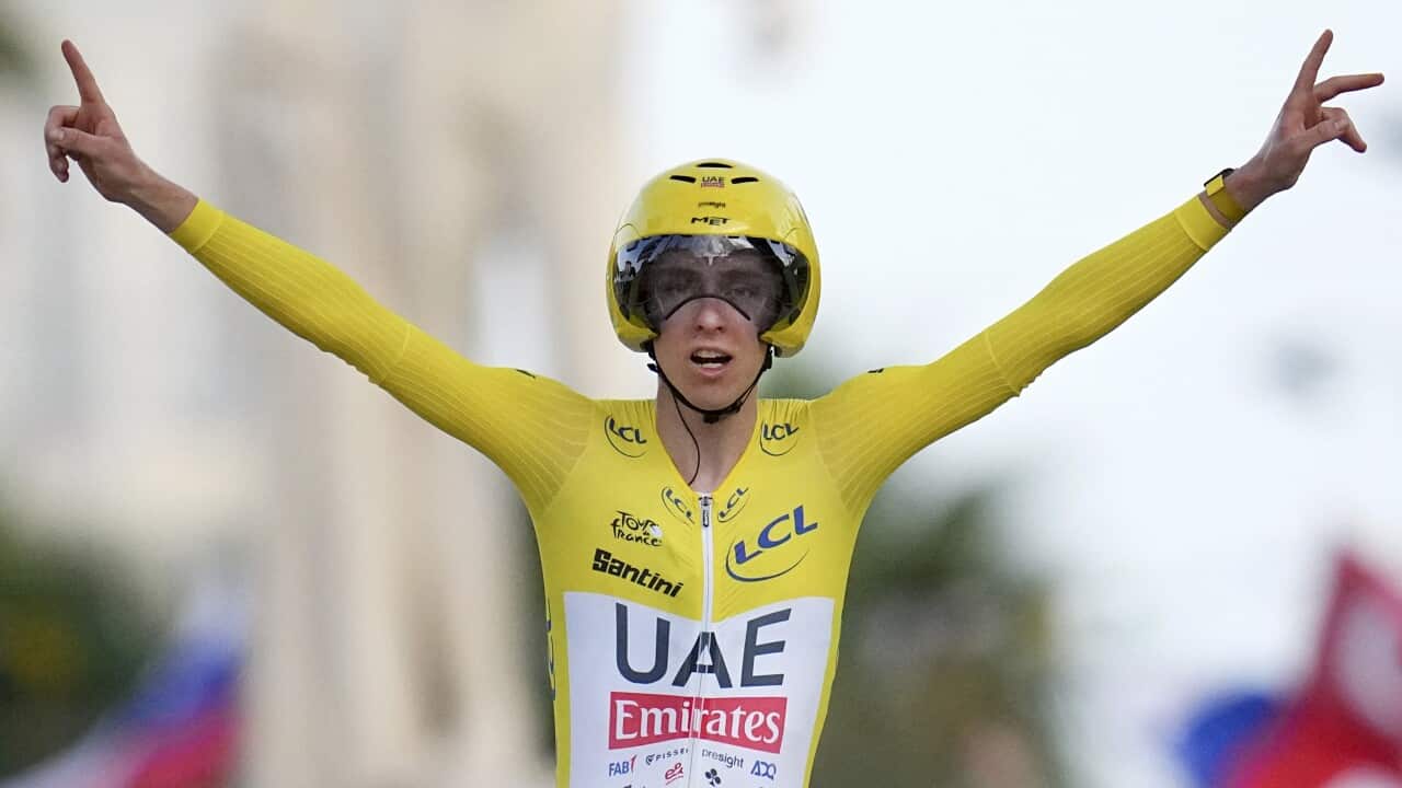 A man in a yellow long-sleeve cycling kit and helmet celebrates with his arms outstretched.
