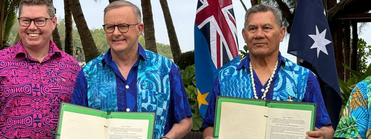 Two men smiling as they each hold a copy of a signed document.