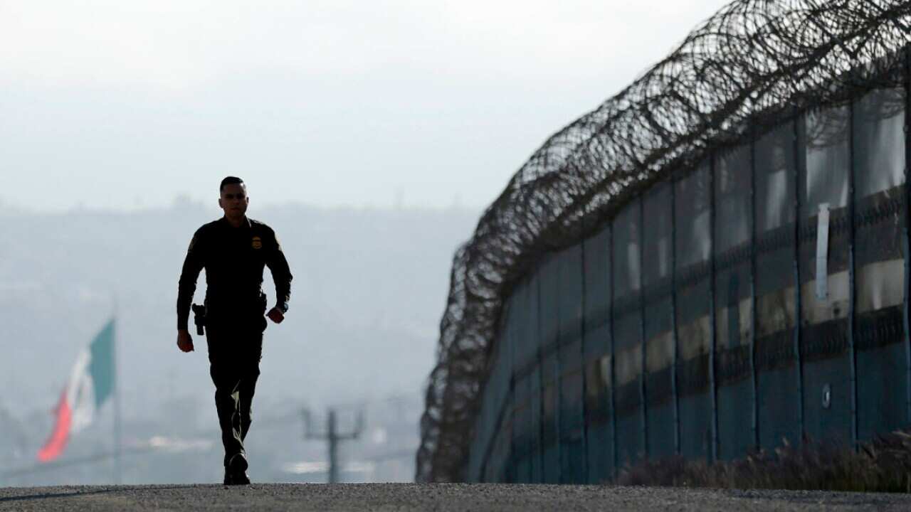 In this June 22, 2016 file photo, Border Patrol agent Eduardo Olmos walks near the secondary fence separating Tijuana, Mexico, background, and San Diego in San Diego.