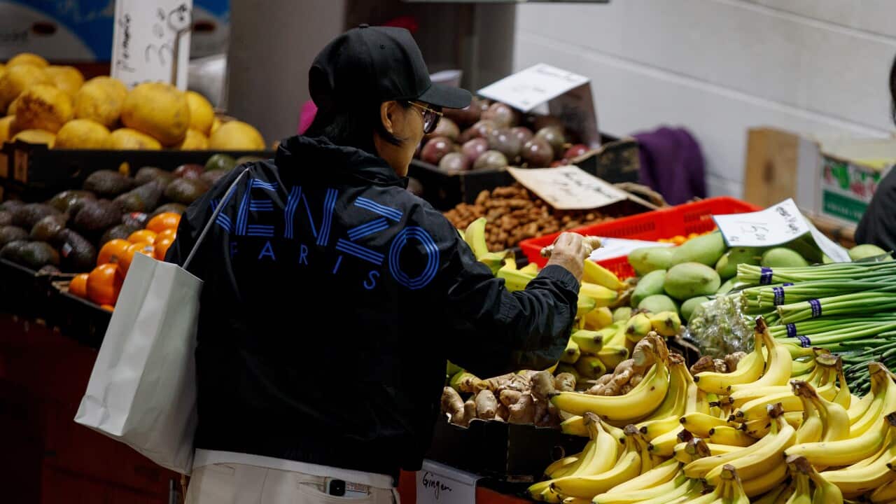 A woman reaches for bananas at a fruit and vegetable market.