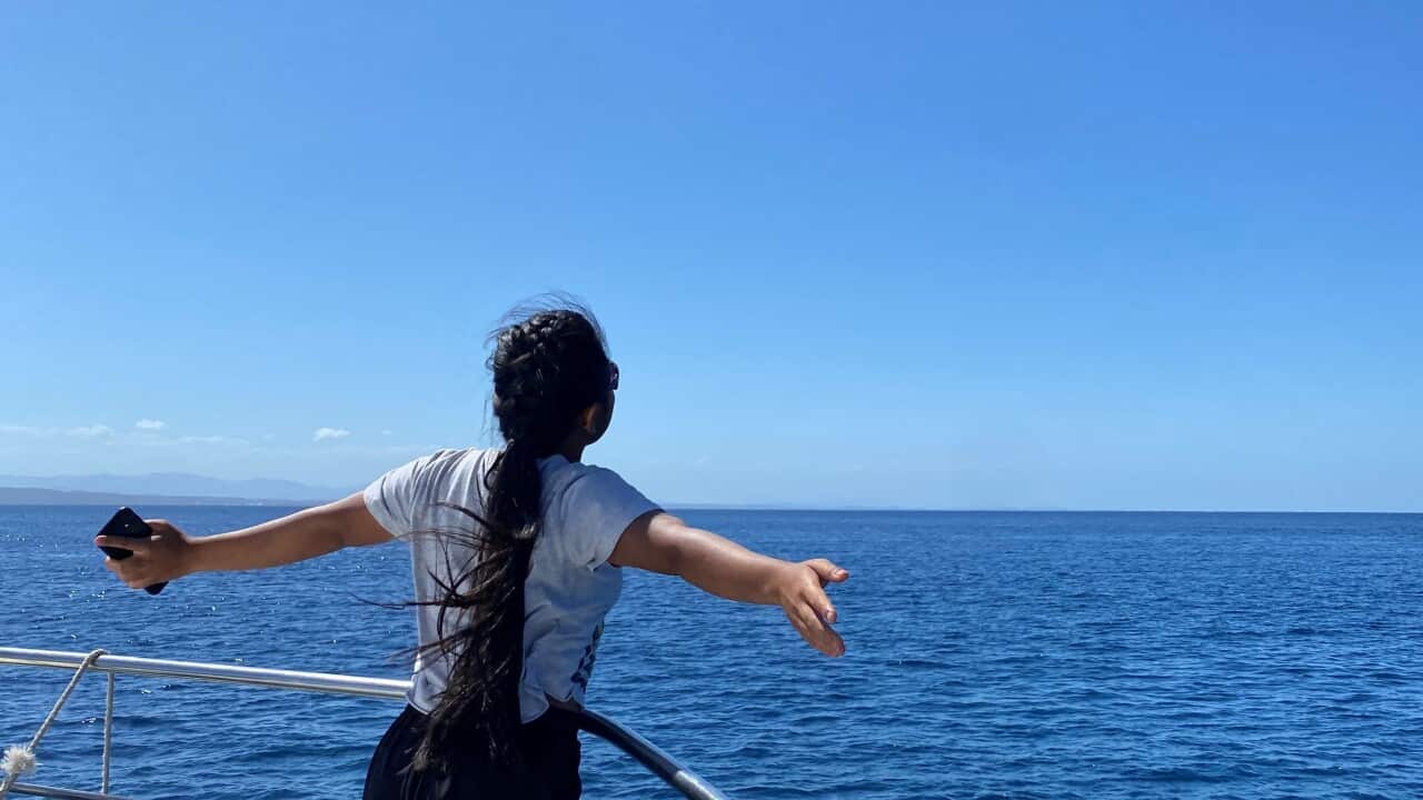 A teenage girl standing on a boat in the ocean, facing away from the camera.