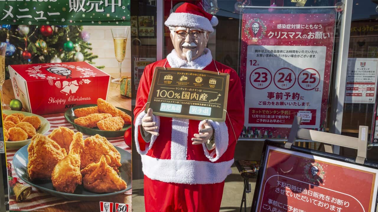 A poster of fried chicken next to a man in a red and white Santa suit holding a sign in Japanese