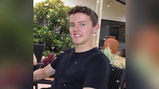 A photo of Jeremy Webb. He is sitting in a garden dressed in a black t-shirt, smiling at the camera.