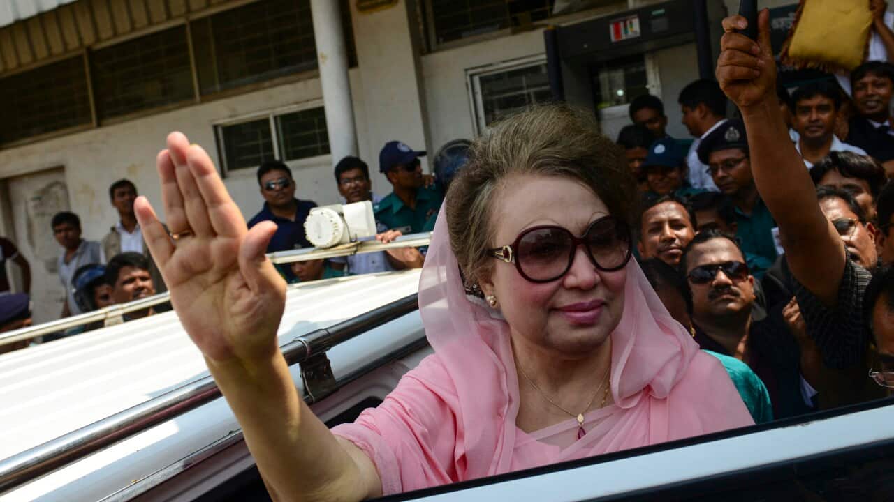 A woman wearing sunglasses in a pink saree waves at a crowd as she enters a car. She is surrounded by a crowd.