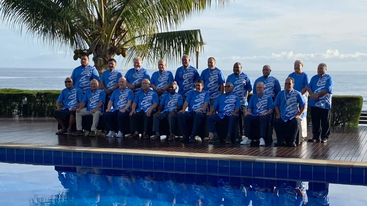 Men wearing blue t-shirts pose for a photo in front of a pool
