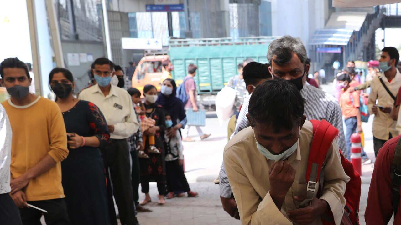 Indian commuters wait in a queue to register as health workers take nasal swab samples from commuters to test for COVID-19