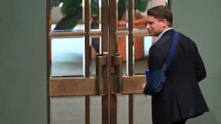 A man in a suit with his left arm in a blue sling walks toward a set of large, ornate double doors.
