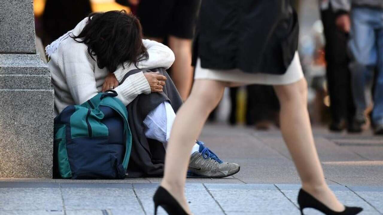 A homeless woman sits on a street corner