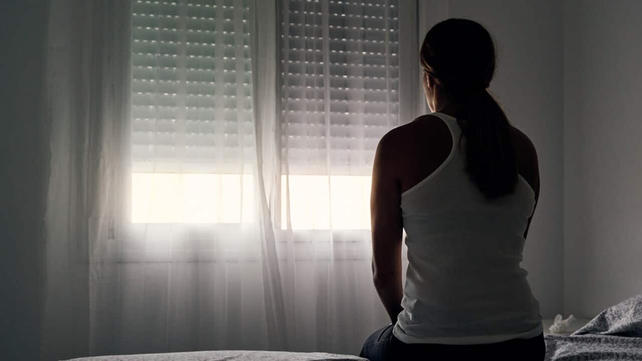 Rear view of an unrecognizable abused woman sitting on her bed looking out the window.