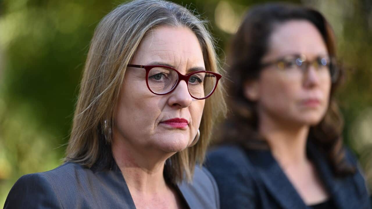 A woman wearing a blazer and glasses with a serious expression