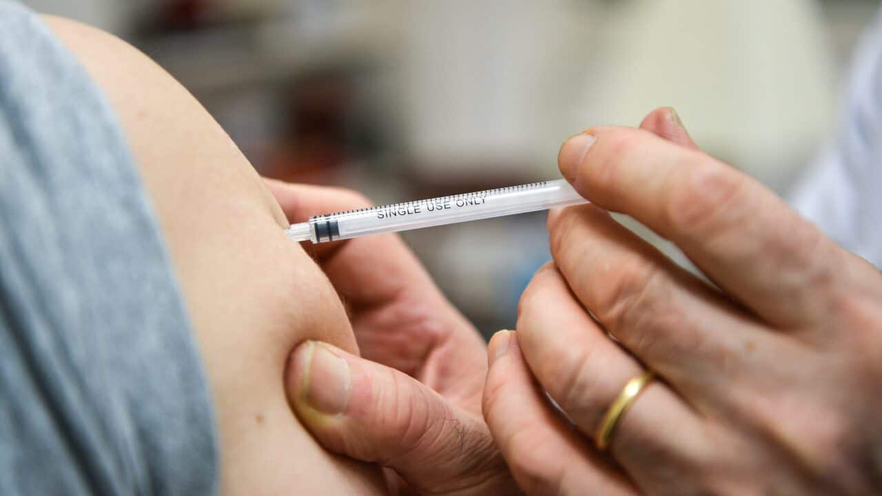 A general practitioner holds a syringe close to the arm of a patient receiving a vaccine booster