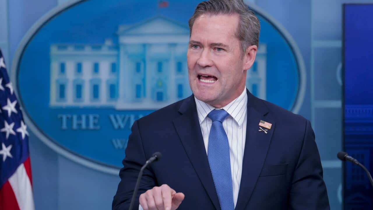 A man in a blue suit and a tie is speaking at a podium.