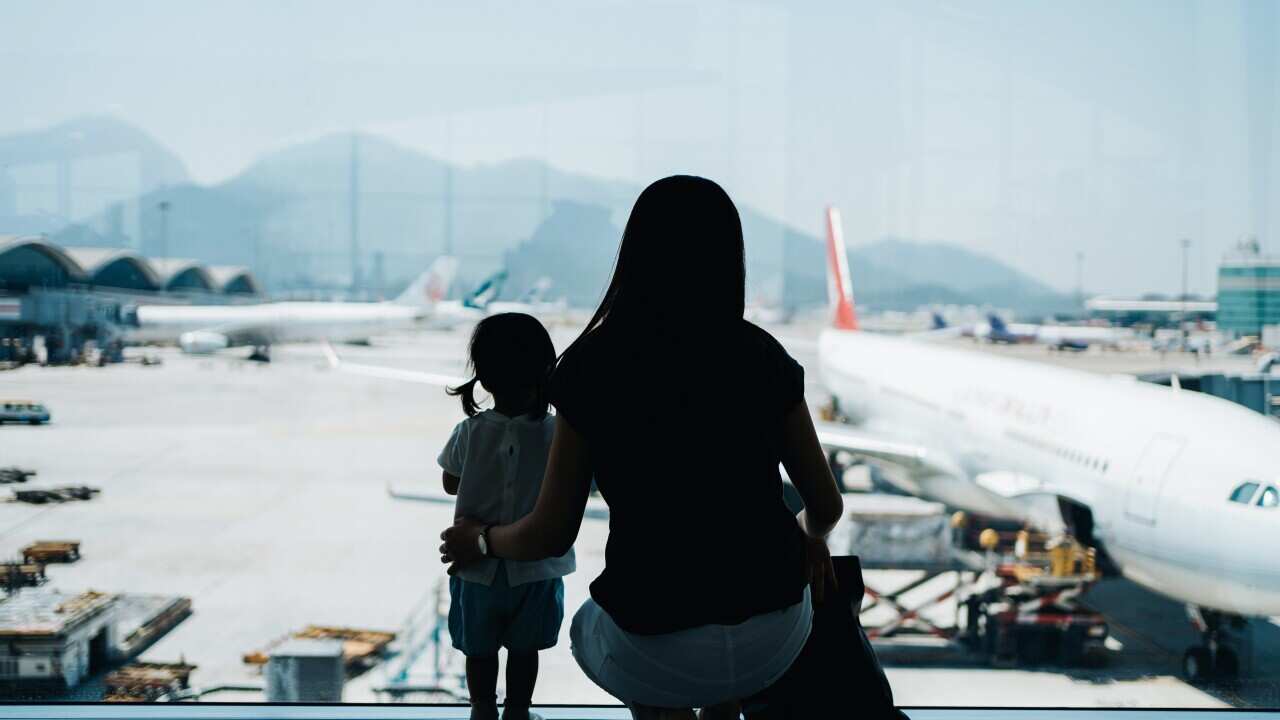 Silhouette of young Asian mother and cute little daughter looking at airplane through window at the airport while waiting for departure. Family travel and vacation concept