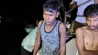 Two men sit in the dark on the edge of a boat, one without a shirt.