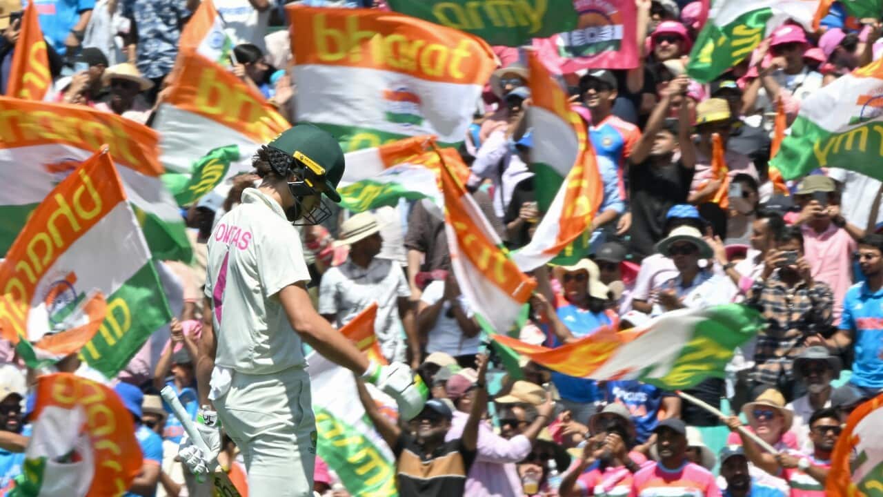 A cricket player is on the field during a test match, with fans in the background, and some are waving Indian flags.