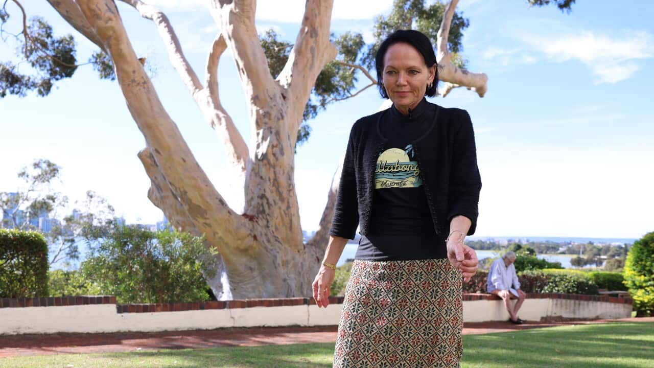 A woman in a black top and patterned skirt walking in front of a tree