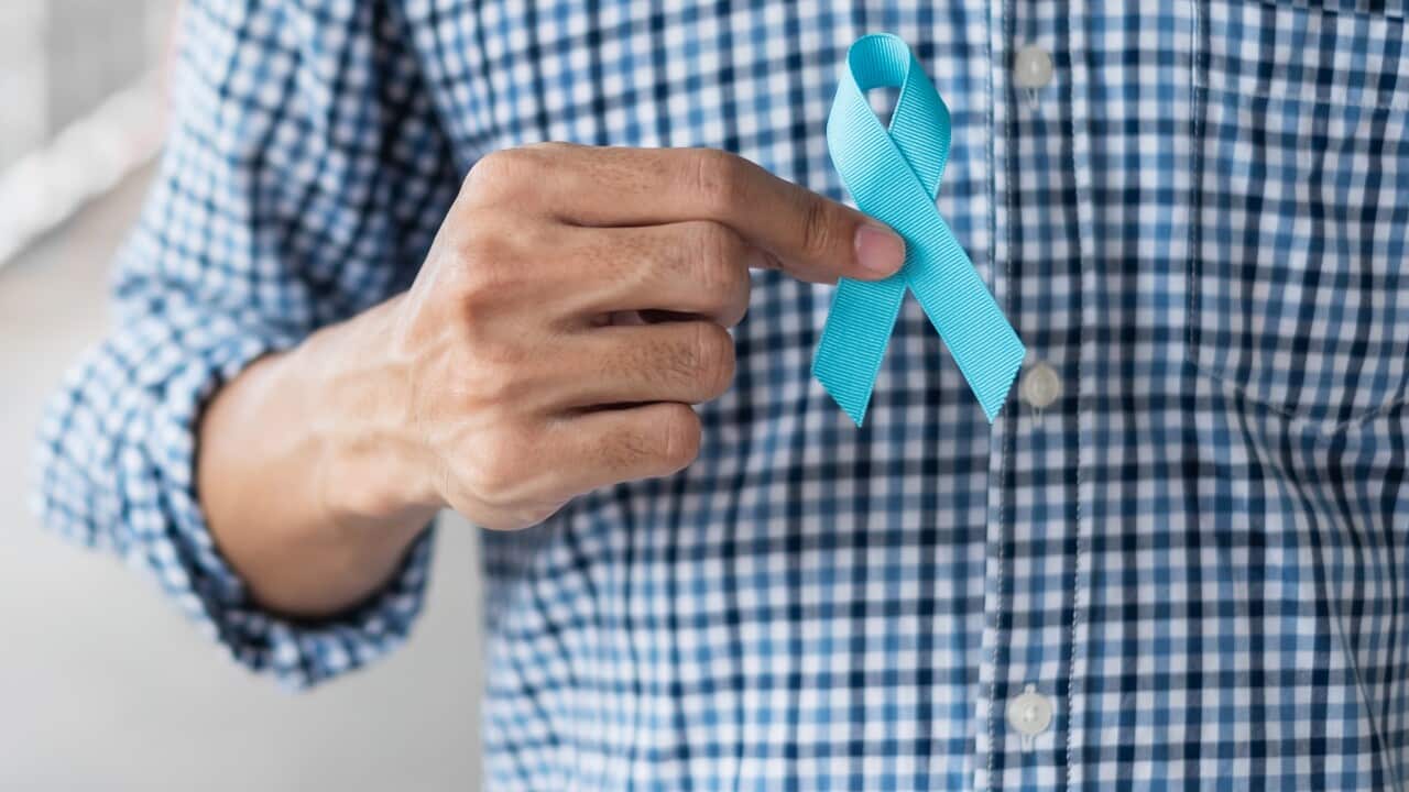 A man holding a blue ribbon for prostate cancer awareness.