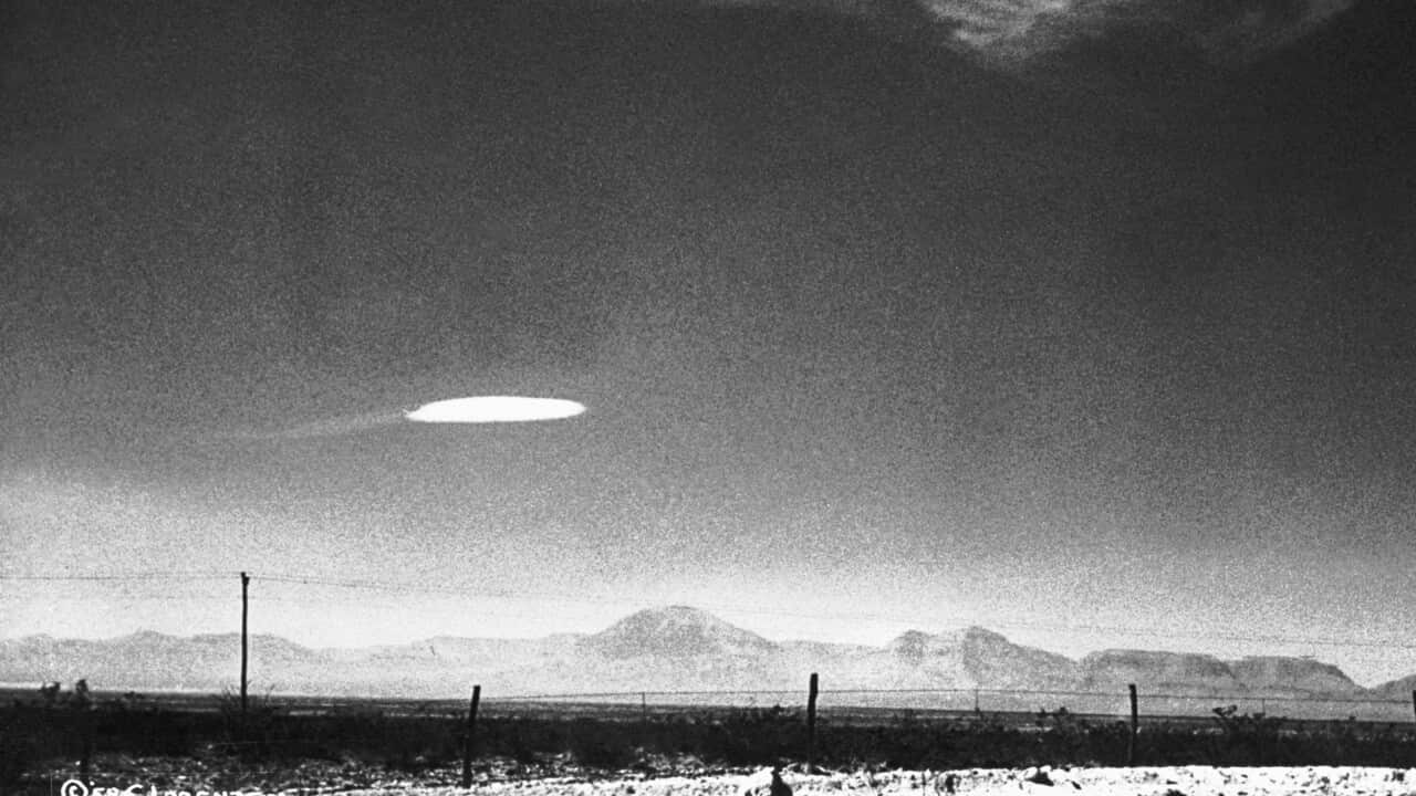 Black and white picture of a glowing white disk flying over a desert area