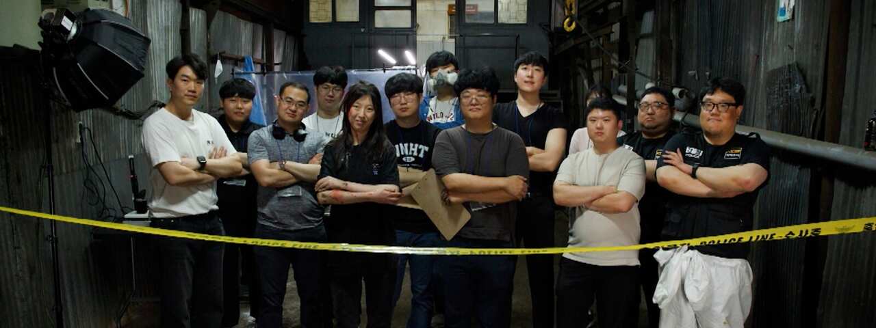 A group of young men and women stand inside a shed-like building behind police tape with their arms folded.