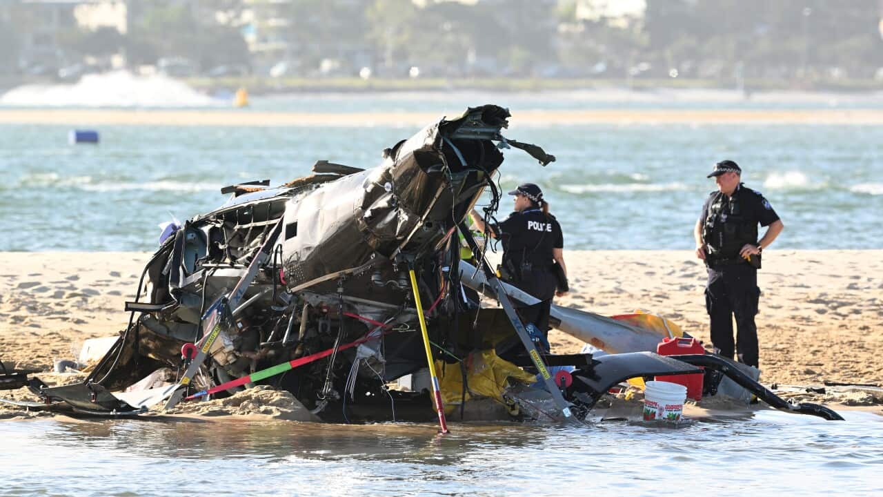 The wreckage of a helicopter on the sand near a beach with two police officer standing nearby.