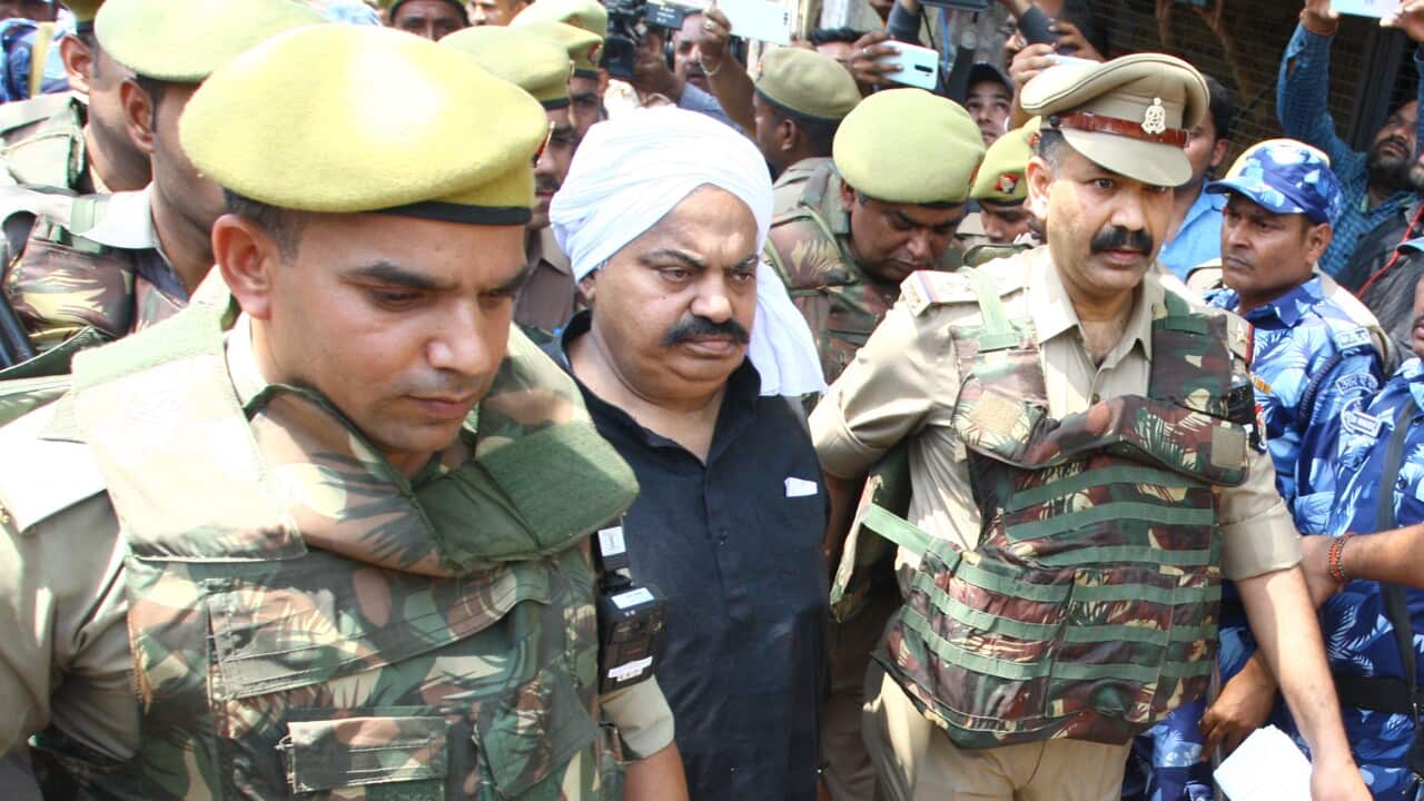 Two men in police uniforms escort a man wearing a white turban through the crowds.