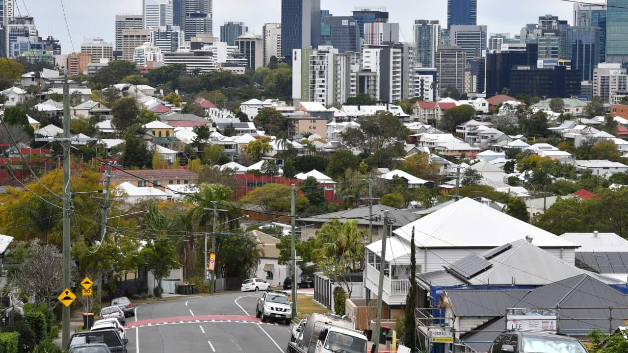 A street with several houses and cars and skyscrapers in the background