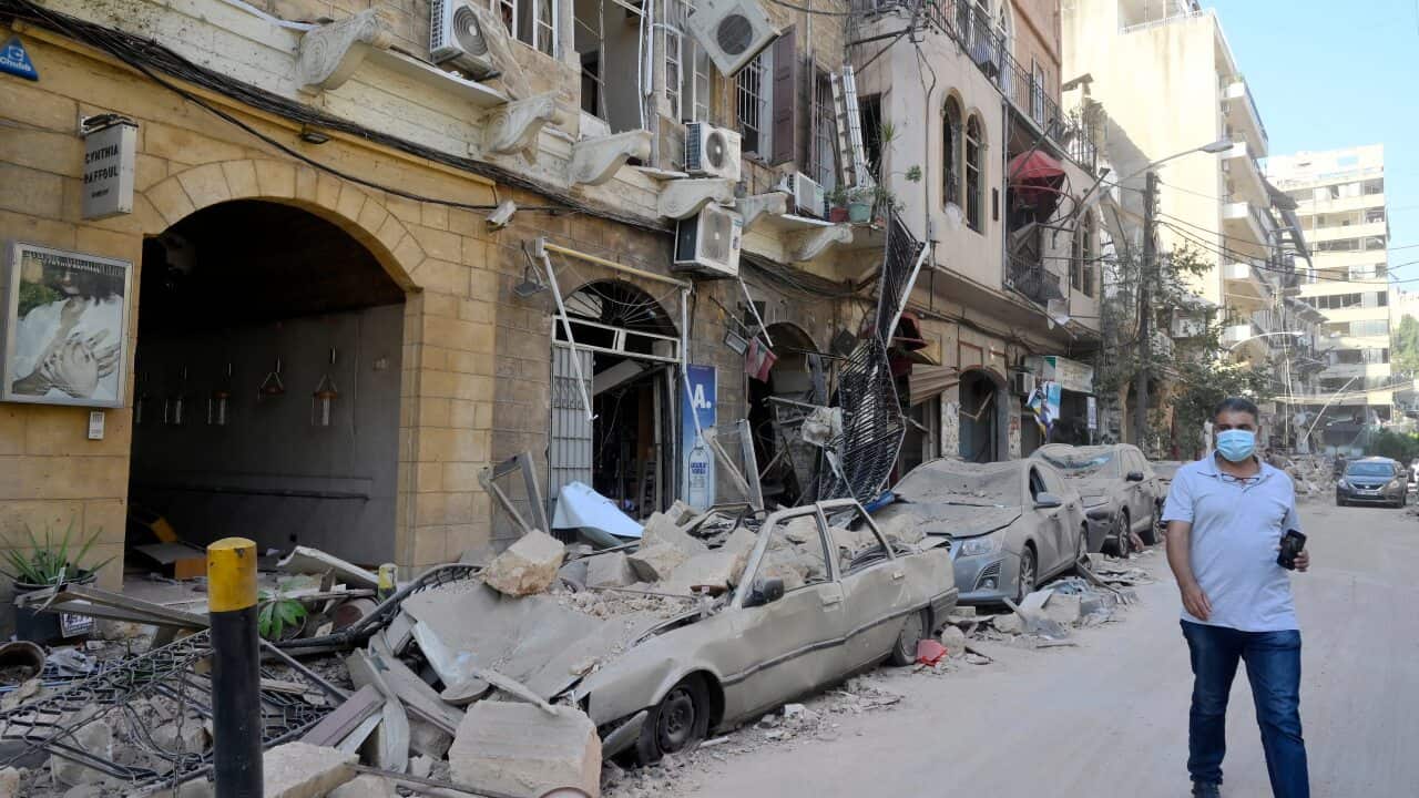 A man walks next to damaged vehicles in the aftermath of a massive explosion in Beirut.