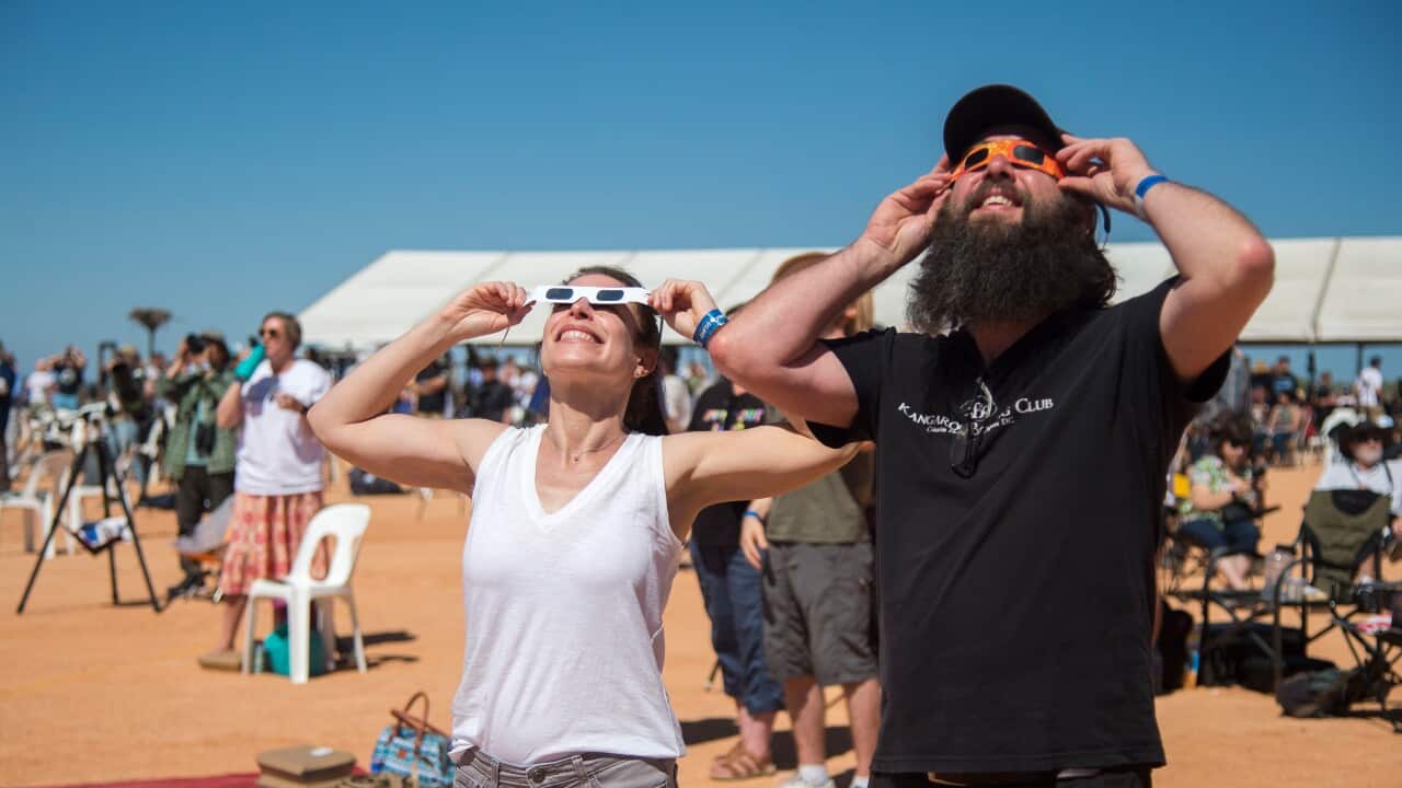 People using special dark eyewear look up at the sky