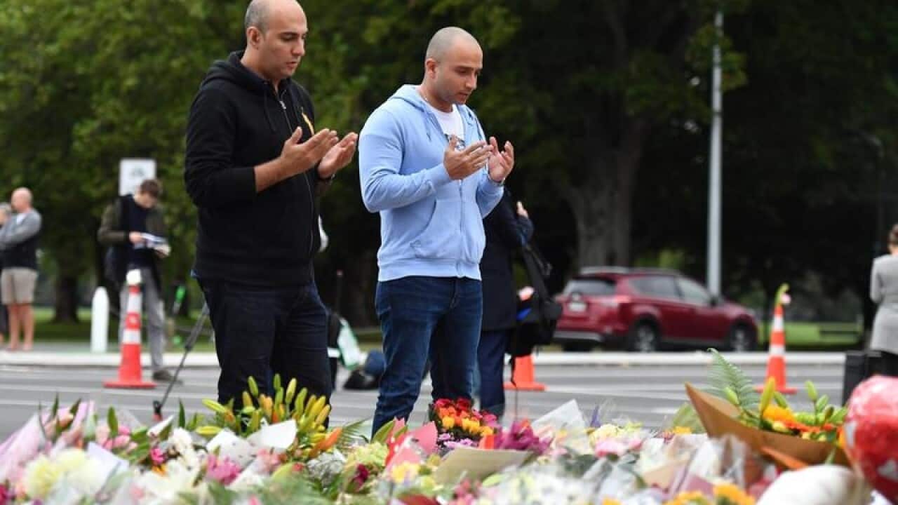 Two men pray at a flower memorial near the Al Noor Masjid.