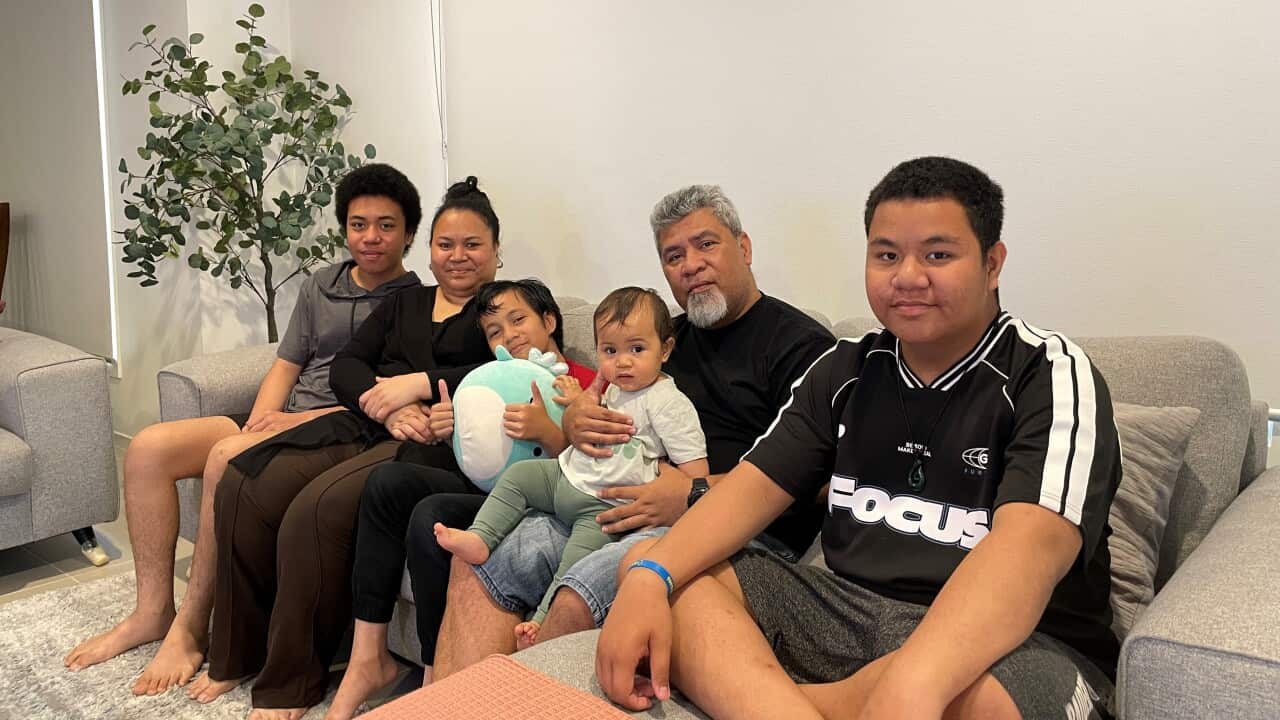 The Manuella family sit in the living room, smiling to the camera