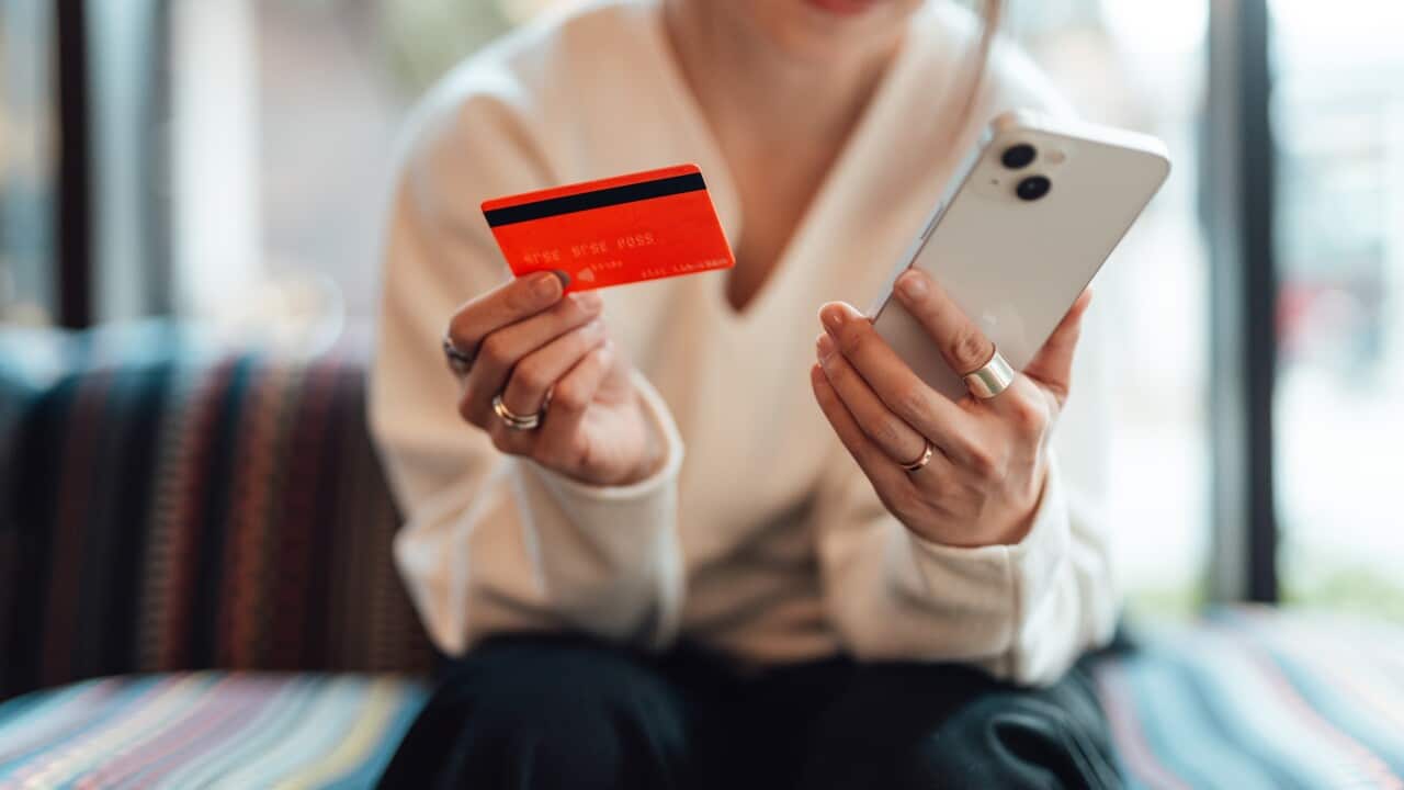A woman holding an orange bank card in one hand and a smartphone in the other.