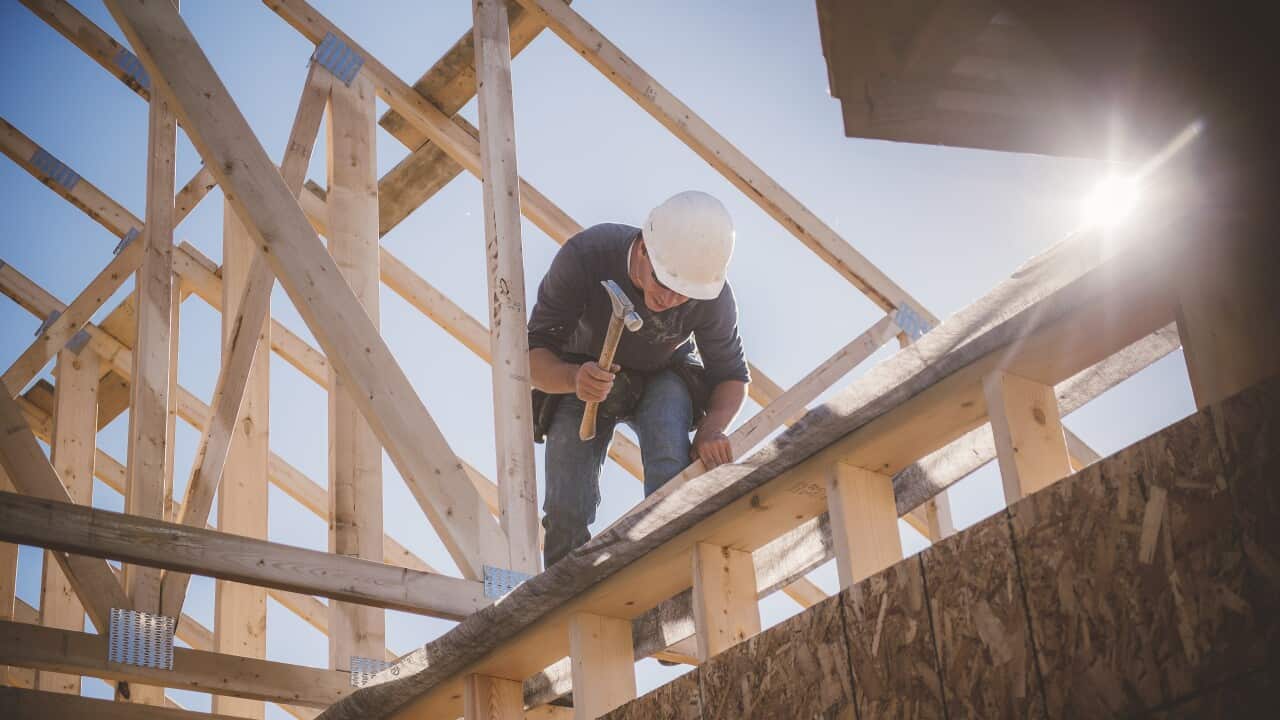 Builder working on rooftop frame of building