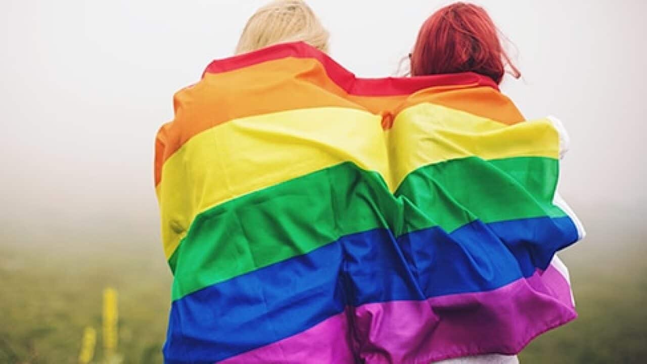 Two people wrapped in the LGBTIQ+ rainbow flag.