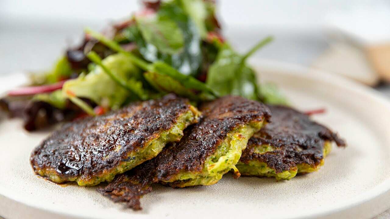 Three green fritters sit on a plate, with a pile of salad leaves.