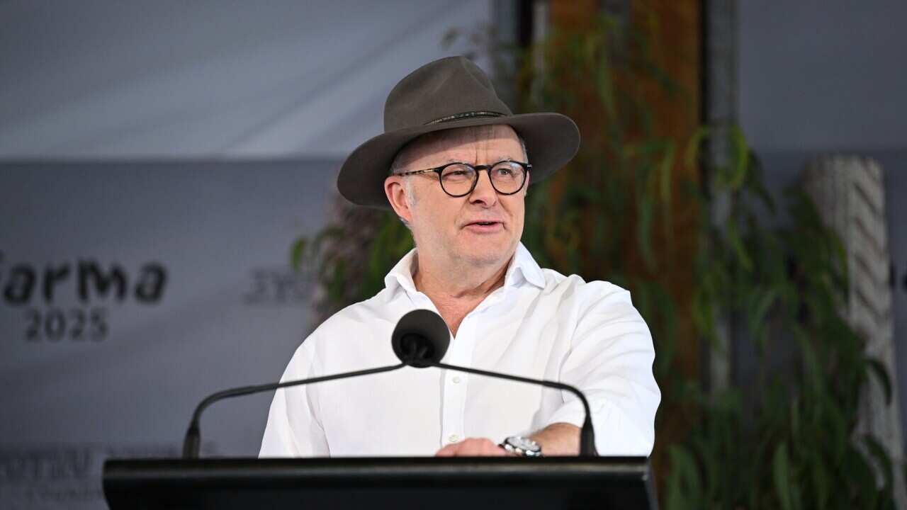 A man wearing a white shirt and hat speaks at a podium.