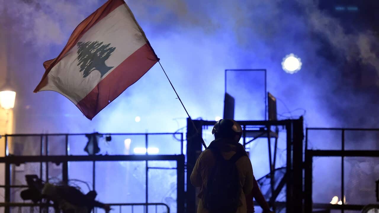 An anti-government protester waves a Lebanese flag during protests and clashes with police outside the Lebanese Parliament building.