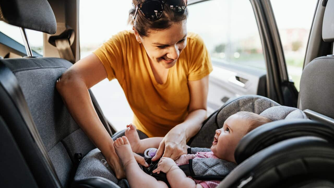 Mother putting baby girl in child seat in the car