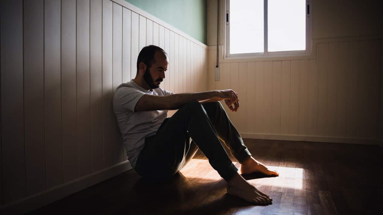 Lonely man sitting on floor by wall in dark room feeling sad