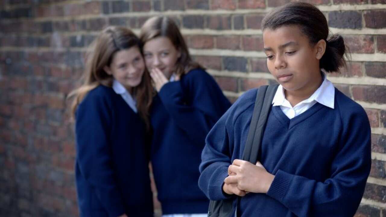 Two school girls (11-12) whispering and laughing at another girl (12-13), focus on front girl