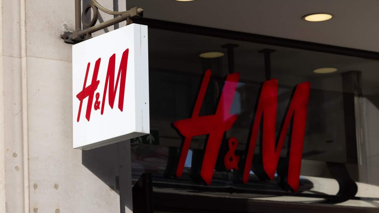 A white sign with red letters of H&M outside a shop front. In a window is larger H&M letters.